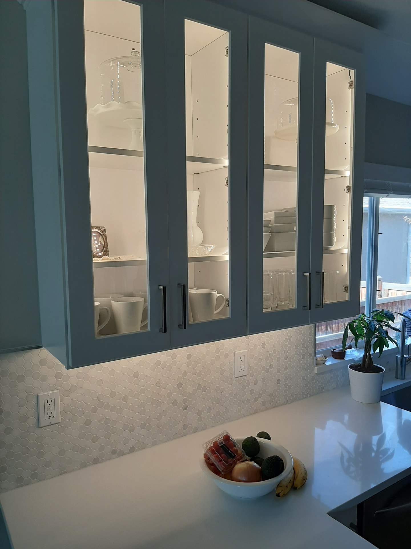 White quartz countertop below glass-front upper cabinets and a hexagon marble backsplash