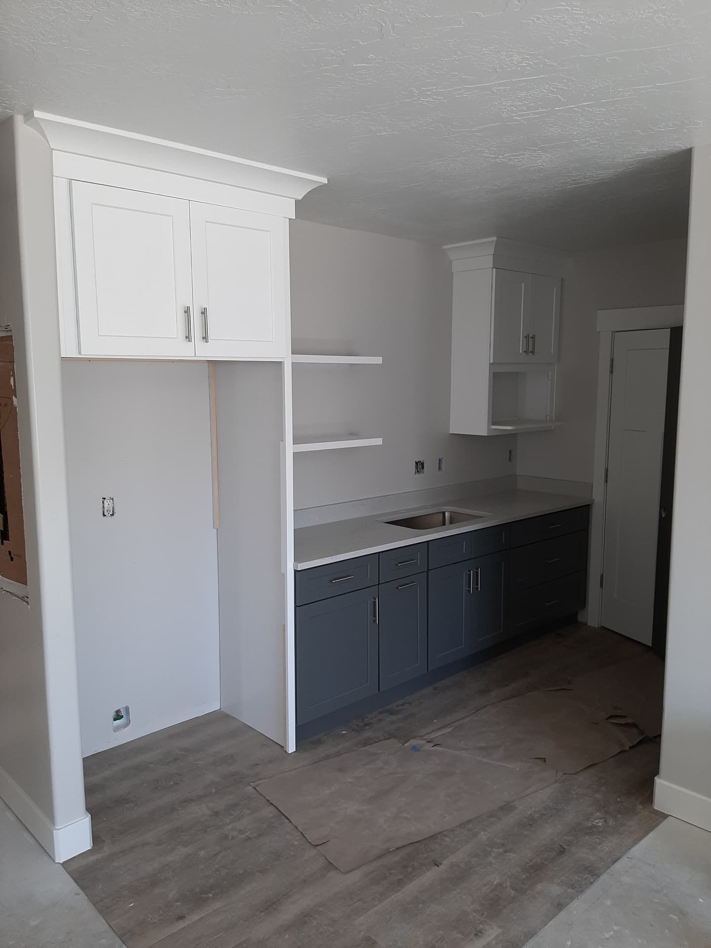 Wide-plank vinyl flooring running beneath navy and white kitchenette cabinetry