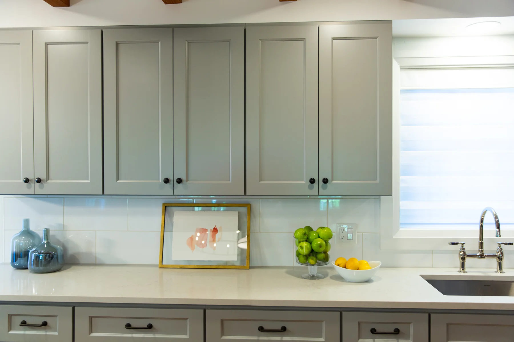 Detailed view of full-height light shaker kitchen cabinets, glass backsplash and sink run