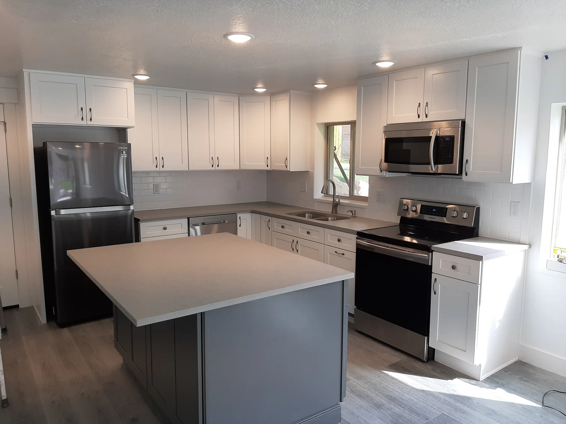 Compact white shaker kitchen with a dark island, light counters and stainless appliances