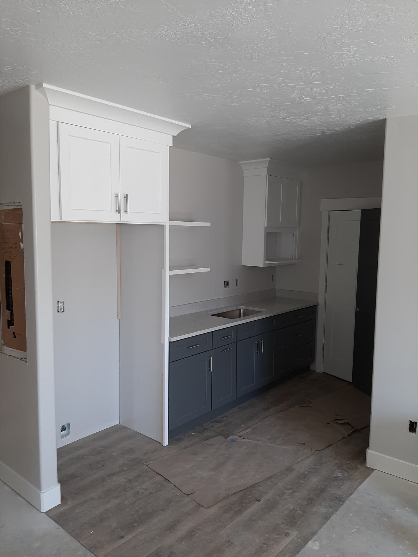 Second view of the same two-tone kitchenette showing the tall white cabinet, open shelving and vinyl plank flooring